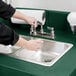 A person using a green Cambro CamKiosk portable hand sink with a metal handle.