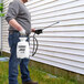 A man using a Chapin disinfectant sprayer on the side of a house.