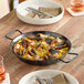 A Vigor enameled carbon steel paella pan filled with seafood rice on a table.