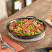 A Vigor enameled carbon steel paella pan of food on a table.