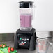 A Waring commercial blender with a strawberry and a purple smoothie in it.