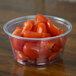 A clear Fabri-Kal plastic deli container filled with tomatoes on a table.