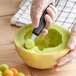 A gloved hand using a Mercer Culinary melon baller to cut a melon.