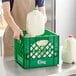 A man holding a jug of milk in a green Choice square milk crate.