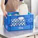 A man holding a blue Choice rectangular milk crate full of milk.