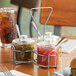 A wire condiment caddy with three clear plastic jars with lids and a spoon inside one jar.