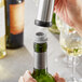 A person using an Acopa gray vacuum wine stopper to pour wine into a bottle.