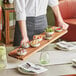 A waiter holding an Acopa acacia wood serving board with food on it.