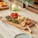 An Acopa acacia wood serving board with cheese, crackers, and olives on it.
