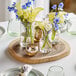 An Acopa round acacia wood serving board on a table with vases of flowers.