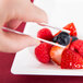 A person holding white plastic tongs over a plate of blueberries and strawberries.
