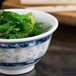 A blue Thunder Group Blue Dragon melamine bowl filled with green seaweed on a table.