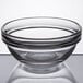 An Arcoroc clear glass ingredient bowl with a rim on a reflective surface.