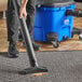 A person using a Lavex Pro blue and black wet/dry vacuum with a black tube to clean carpet.