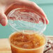 A hand placing a New Roots PLA compostable plastic lid on a plastic cup of iced coffee.