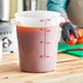 A woman using a measuring cup to pour tomato sauce into a Carlisle white food storage container on a counter.