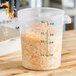 A hand measuring shredded cheese into a Carlisle translucent plastic food storage container.
