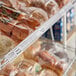 A shelf with plastic-wrapped food items labeled with a 44" x 1 1/4" clear clip-on label holder.