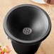 A black Acopa stainless steel wine tasting spittoon lid with a hole in it over a black bucket.