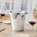 A silver Acopa wine tasting spittoon on a table with wine glasses and flowers.