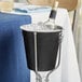 A wine bottle in a black stainless steel bucket with ice.