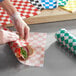 A person in gloves wrapping a sandwich in green and white checkered paper.