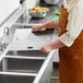 A person in an apron cutting a piece of stainless steel over a sink.