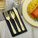 A black napkin with a Visions gold fork and spoon on top.