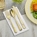 A Visions heavy weight gold fork and knife on a white napkin next to a plate of food.