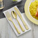 A white linen pocket fold napkin with Visions gold plastic cutlery on a plate of rice.