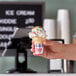 A hand holding a small JOY jacketed cake cone filled with ice cream and sprinkles.