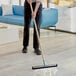 A person using a Lavex Black Neoprene Floor Squeegee with a wooden stick to clean the floor.