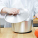 A person in a chef's uniform holding a Vollrath Arkadia lid over a pot.