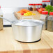 A Vollrath stainless steel pot with a lid on a wooden cutting board.