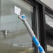A Lavex window cleaner with a blue and white mop attached to the handle cleaning a window.
