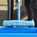 A person using a blue Lavex window cleaning mop with a sponge to clean a window.