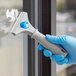 A hand in blue gloves using a Lavex glass scraper to clean a window.