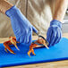 A person in blue Noble biodegradable nitrile gloves using tongs to cut a crab claw.