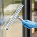 A person wearing blue gloves using a Lavex window squeegee to clean a window.