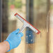 A person wearing a blue glove uses a Lavex window squeegee to clean a window.