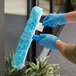 A person wearing blue gloves using a Lavex Pro window cleaning kit to clean a window.