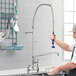 A man using a Waterloo pre-rinse faucet to wash dishes in a professional kitchen.