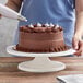 A woman using an Ateco plastic cake turntable to decorate a chocolate cake with white frosting.