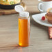 An 8 oz. clear cylinder sauce bottle of honey with a white cap on a table.