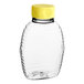 A clear plastic bottle with a yellow lid containing honey.