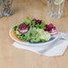 A GET Barcelona Diamond wide rim melamine plate with a salad and a fork on it on a table with a napkin and a glass.