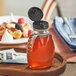A Classic Queenline PET honey bottle with a black flip top lid on a wooden tray with food.