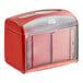 A red Tork tabletop napkin dispenser with clear plastic lid on a counter.