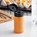 A clear cylinder sauce bottle with a black lid filled with orange liquid.