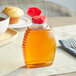 A Classic Queenline PET honey bottle with a red cap of honey on a table next to a muffin and a cup of tea.